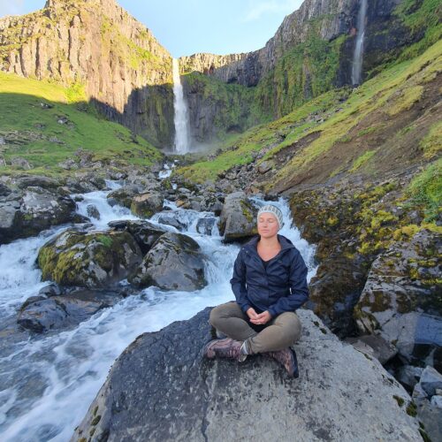 Woman traveller meditating next to waterfall in Iceland